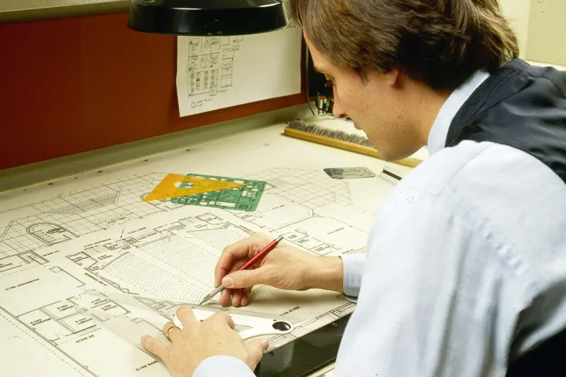 An old photo of a Thomas employee working on a set of construction plans
